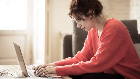 Junge Frau arbeitet zuhause an ihrem Laptop