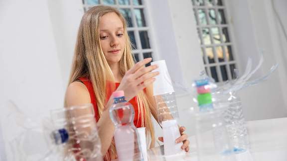 Ein Mädchen bastelt mit Kunststoffflaschen und Einwegbechern.