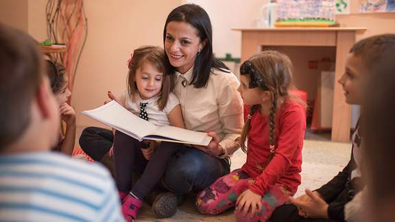 Erzieherin liest einer Gruppe von Kindern im Kindergarten eine Geschichte vor.