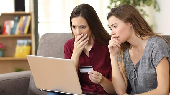 Zwei Frauen blicken erschrocken auf einen Laptop, eine hält eine Karte in der Hand