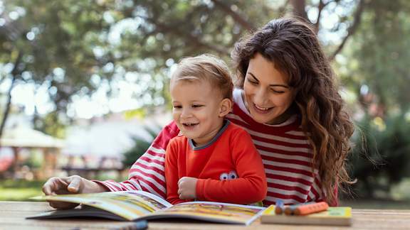 Eine Mutter liest ihrem Kleinkind im Freien aus einem Bilderbuch vor