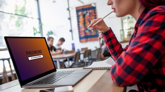 Seitenansicht einer jungen Frau, die im Café vor der Passworteingabe ihres Laptops sitzt. 