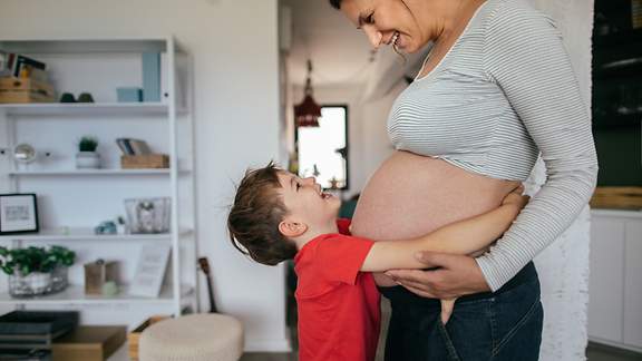 Vorschulkind umarmt seine schwangere Mama.