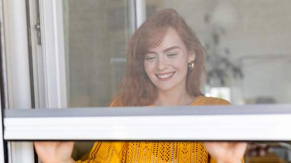 Eine Frau schließt ihr mit einem Moskitonetz geschütztes Fenster