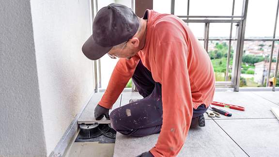 Mann legt Granitfliesen im Freien auf dem Balkon