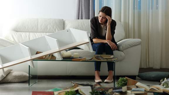 Eine verzweifelte Frau sitzt in ihrer nach einem Einbruch durchwühlten Wohnung