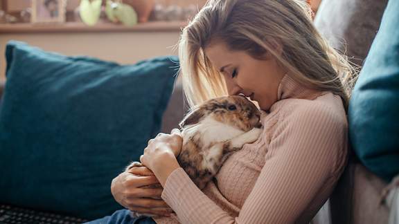 Eine Frau sitzt auf dem Sofa und schmust mit einer Katze