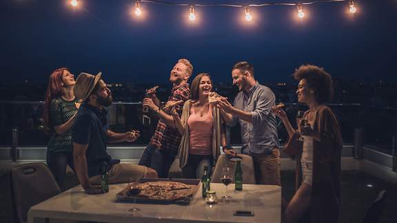 Eine Gruppe junger Menschen veranstaltet nachts auf einer Terrasse eine Feier. 