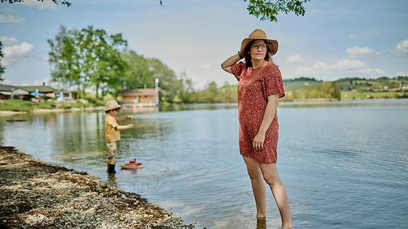 Eine Frau und ihr kleines Kind stehen mit den Füßen im Wasser eines Sees