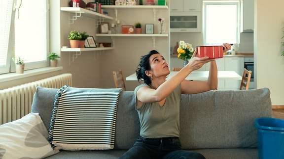 Frau im Wohnzimmer fängt tropfendes Wasser von der Decke mit einem Kochtopf auf.