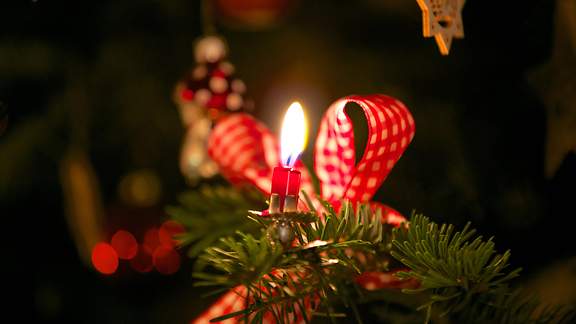 Eine Wachskerze brennt an einem Weihnachtsbaum