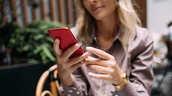 Frau blickt auf ihr rotes Smartphone