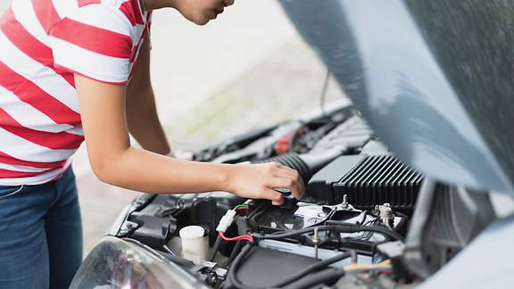 Frau überprüft die Autobatterie ihres Fahrzeuges.