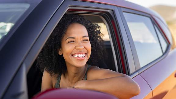 Eine junge Frau lacht aus dem geöffneten Autofenster hinaus