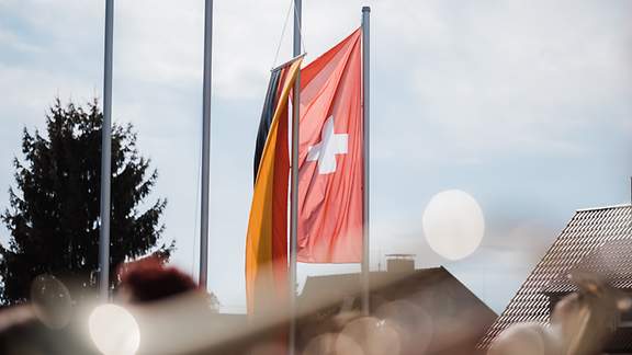 Schweizer und deutsche Flagge wehen nebeneinander am Mast im Wind