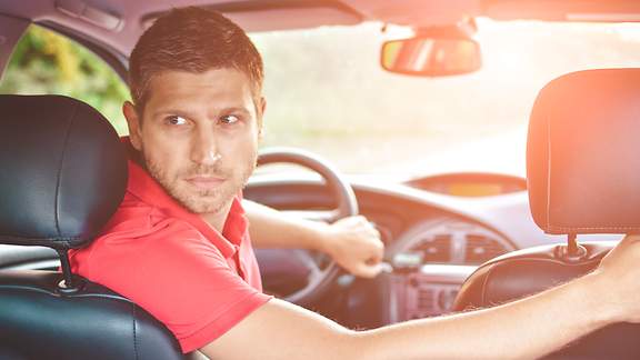 Mann sitzt im Auto und parkt rückwärts ein