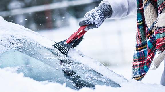 Schnee wird von einer Autoscheibe gekratzt