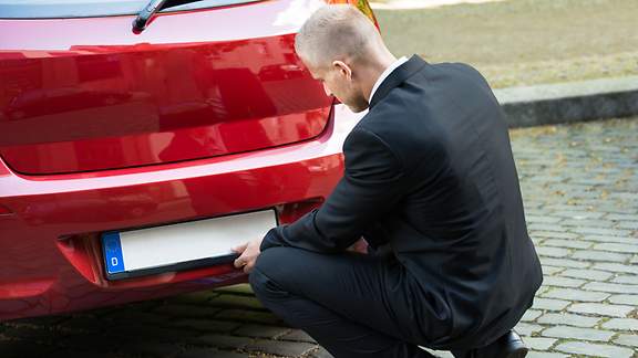 Ein Mann bringt Kurzzeitkennzeichen an seinem Auto an.
