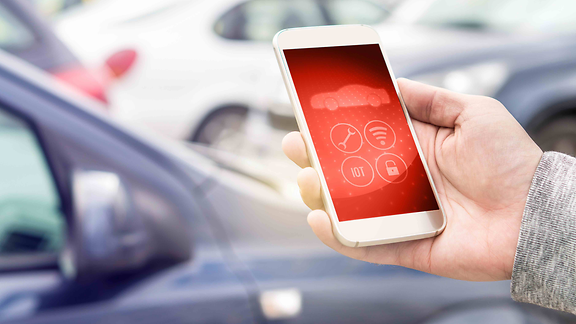 Hand hält ein Smartphone auf einem Parkplatz