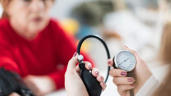 Frau bekommt Blutdruck mit Blutdruckmessgerät von Ärztin gemessen.