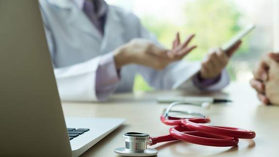 Ein Arzt mit Tablet in der Hand spricht zu einem Patienten