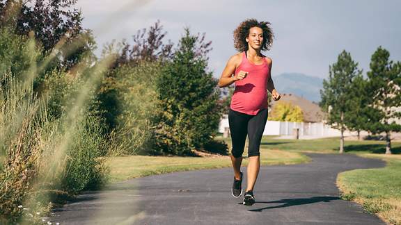 Schwangere Frau joggt durch einen Park