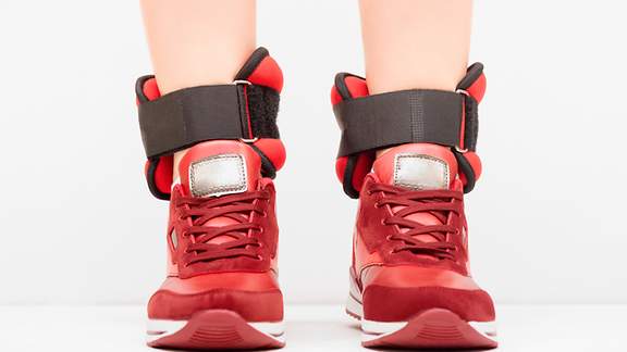Gewichtsmanschetten um die Knöchel einer Joggerin mit roten Schuhen