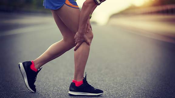 Ein Läufer fasst sich an Oberschenkelmuskulatur und Wade