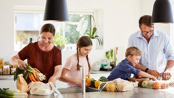 Familie packt in der Küche verschiedene Obst- und Gemüsesorten aus