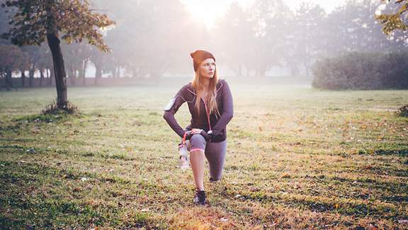 Eine Joggerin dehnt ihre Muskulatur auf einer Wiese