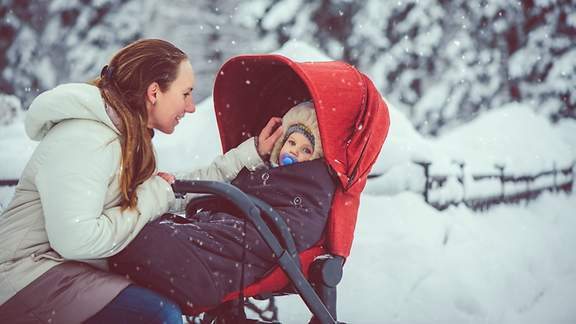 Eine Mutter hockt im Schnee vor ihrem Baby in der Karre
