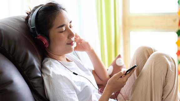 Ein junge Frau hört entspannt Musik mit Kopfhörer.