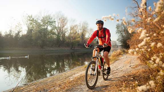 Sportlicher Radfahrer mit Sturzhelm fährt an einem See entlang