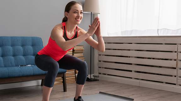 Eine junge Frau macht Gymnastik im Wohnzimmer