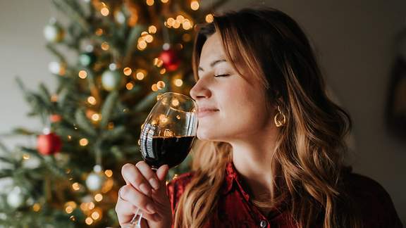 Junge Frau riecht genüßlich vor dem Weihnachtsbaum an ihrem Getränk