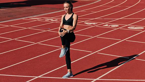 Sprinter-Frau in Sportbekleidung bei Aufwärmübungen vor dem Lauf auf der Stadionbahn mit roter Beschichtung im Freien