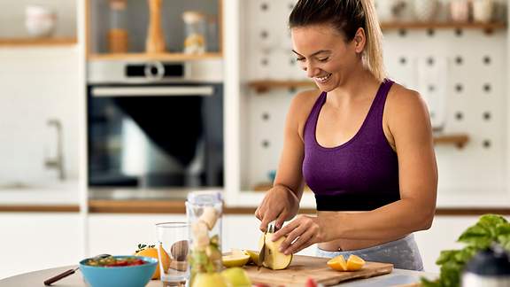 Eine junge Frau im Sportdress bereitet sich in der Küche eine gesunde Mahlzeit zu