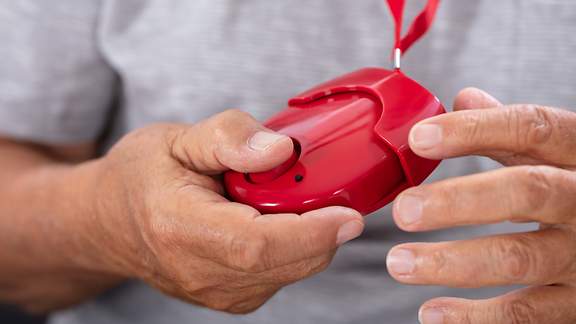 Älterer Mann hält seinen roten Hausnotruf in den Händen