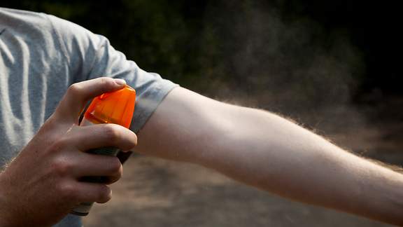 Mann sprüht seine Armbeuge mit Insekten-Abwehrspray ein.