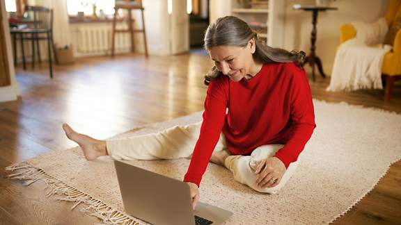 Frau sitzt entspannt auf einem Teppich und recherchiert am Laptop