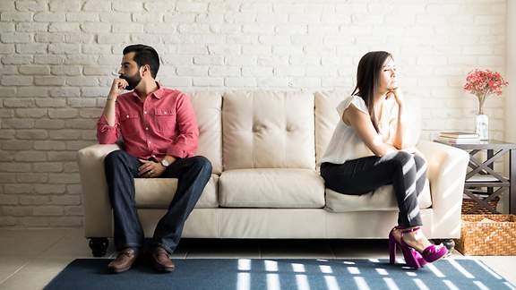 Verärgertes Paar sitzt getrennt voneinander an verschiedenen Enden auf der Couch.