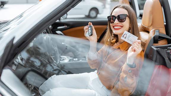 Eine junge Frau zeigt strahlend Autoschlüssel und Führerschein