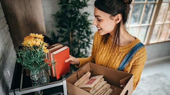 Eine junge Frau packt Bücher in einen Umzugskarton