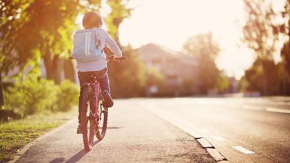 Ein Kind fährt auf seinem Fahrrad an einer Straße entlang.