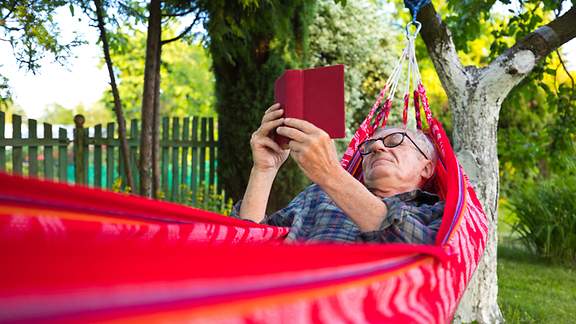 Alter Mann liegt zufrieden in der Hängematte und liest ein Buch