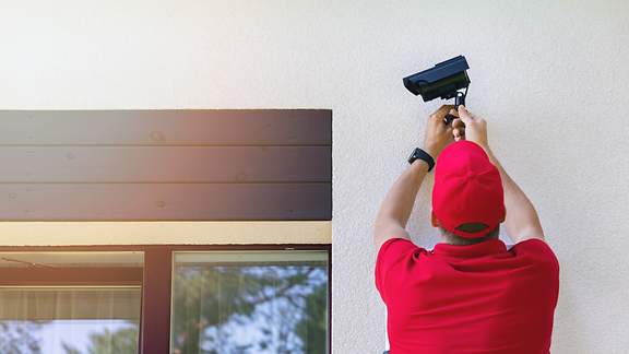 Techniker installiert Außenüberwachungskamera an Hausaußenwand