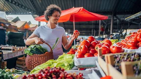 Junger Mann prüft eine Tomate am Gemüsestand auf dem Markt