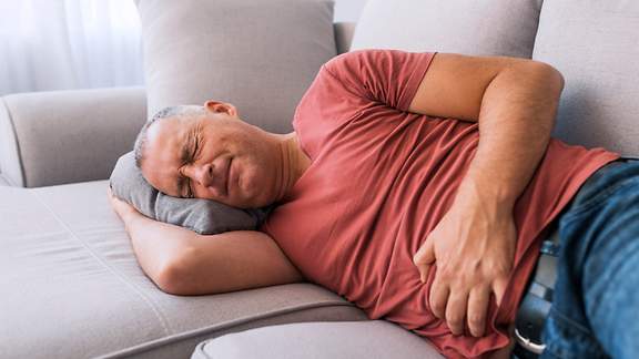 Mann liegt mit Unterleibsschmerzen auf dem Sofa