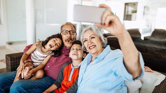 Oma macht mit ihren zwei Enkelkindern und dem Opa ein Selfie auf dem Sofa.