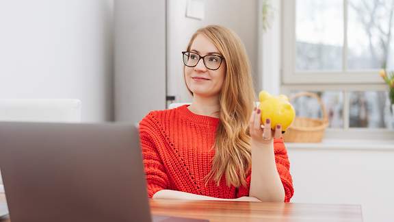 Junge Frau mit Sparschwein vor einem Laptop